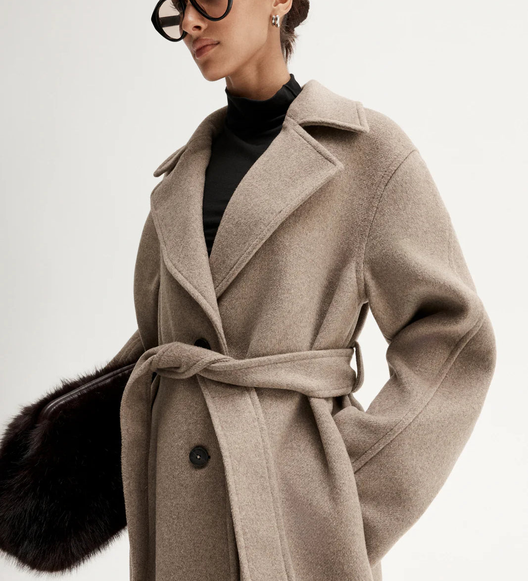 Woman wearing a beige coat with a black background Elka Collective