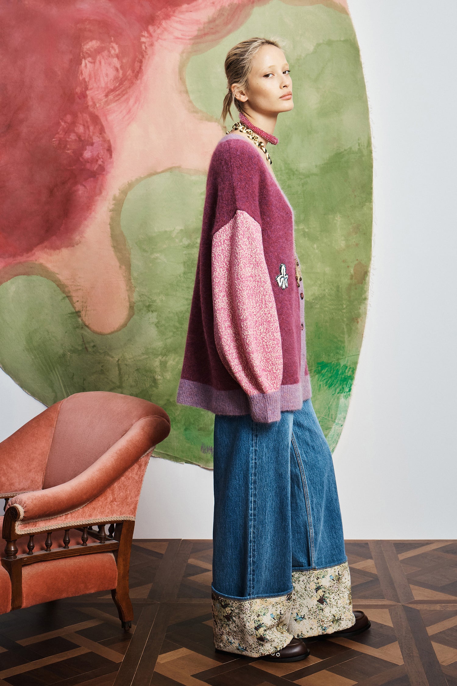 Woman wearing a colorful sweater and jeans standing in front of a painting.