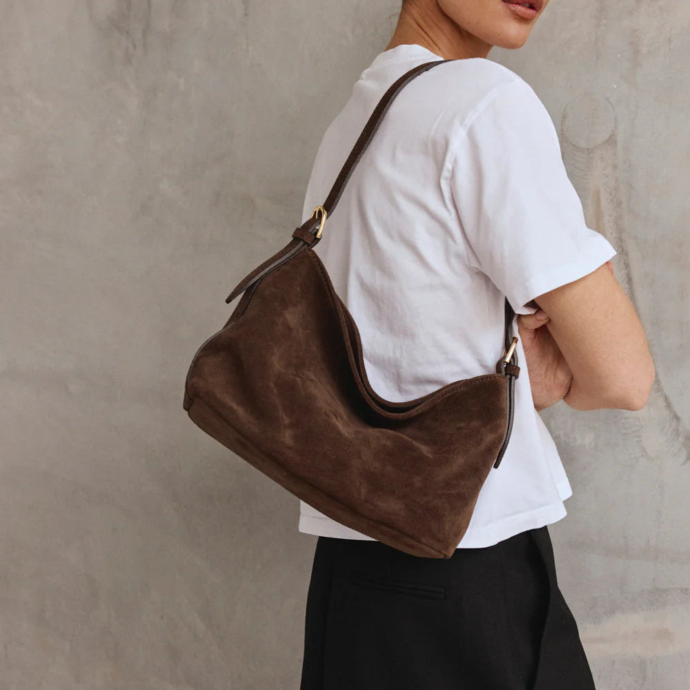 Woman carrying a brown leather handbag against a neutral background