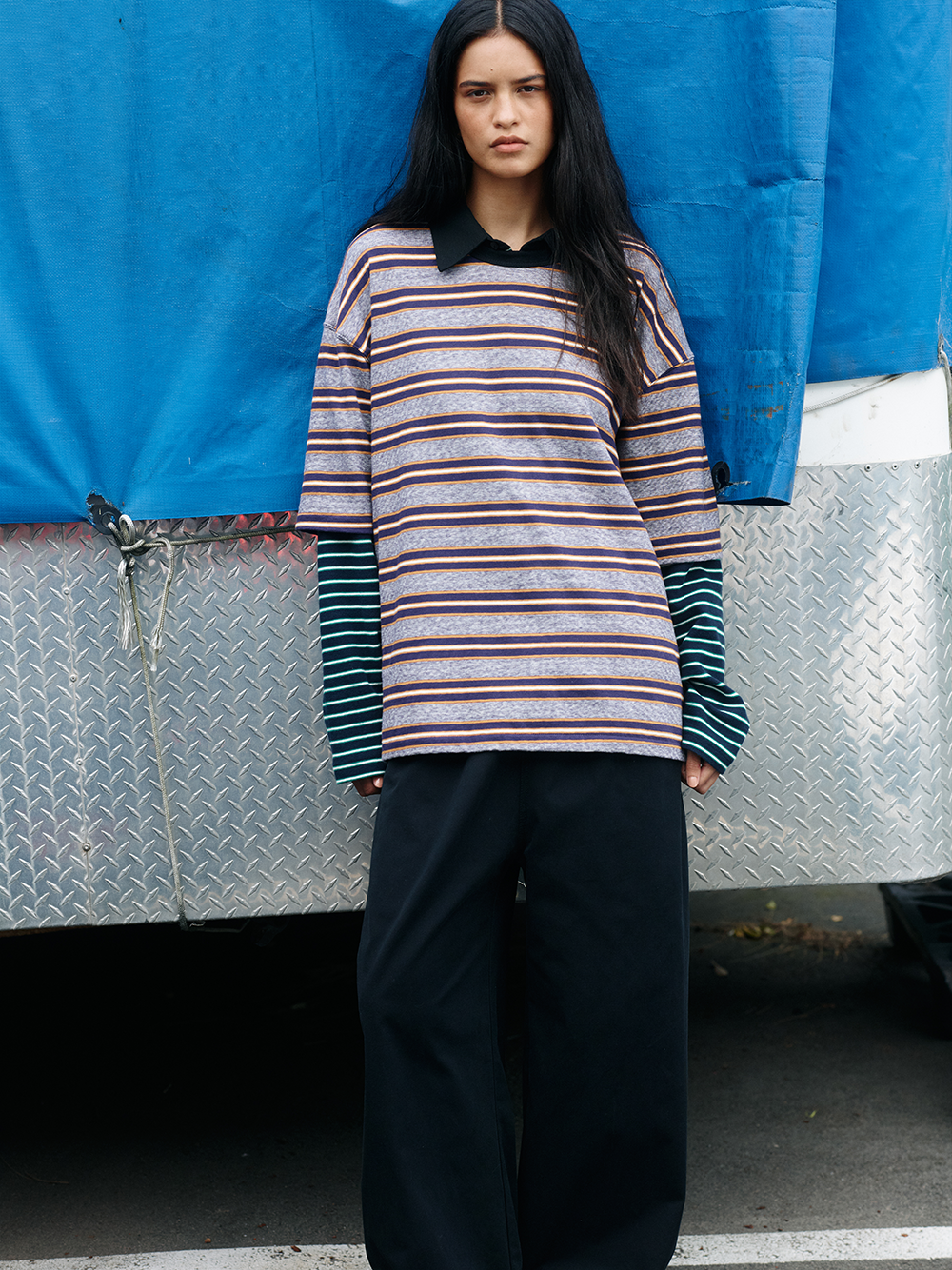 Person wearing a striped sweater and dark pants standing in front of a blue tarp.