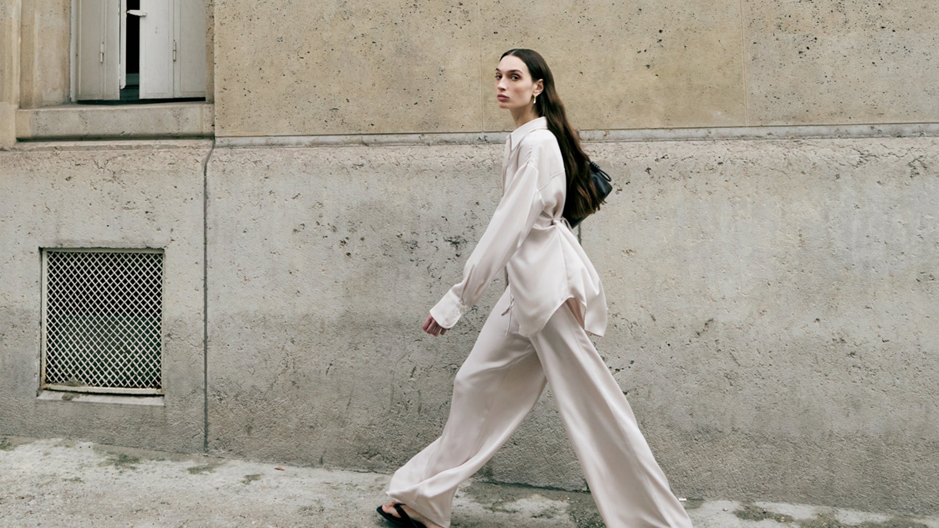 Woman in a white outfit walking past a textured wall.