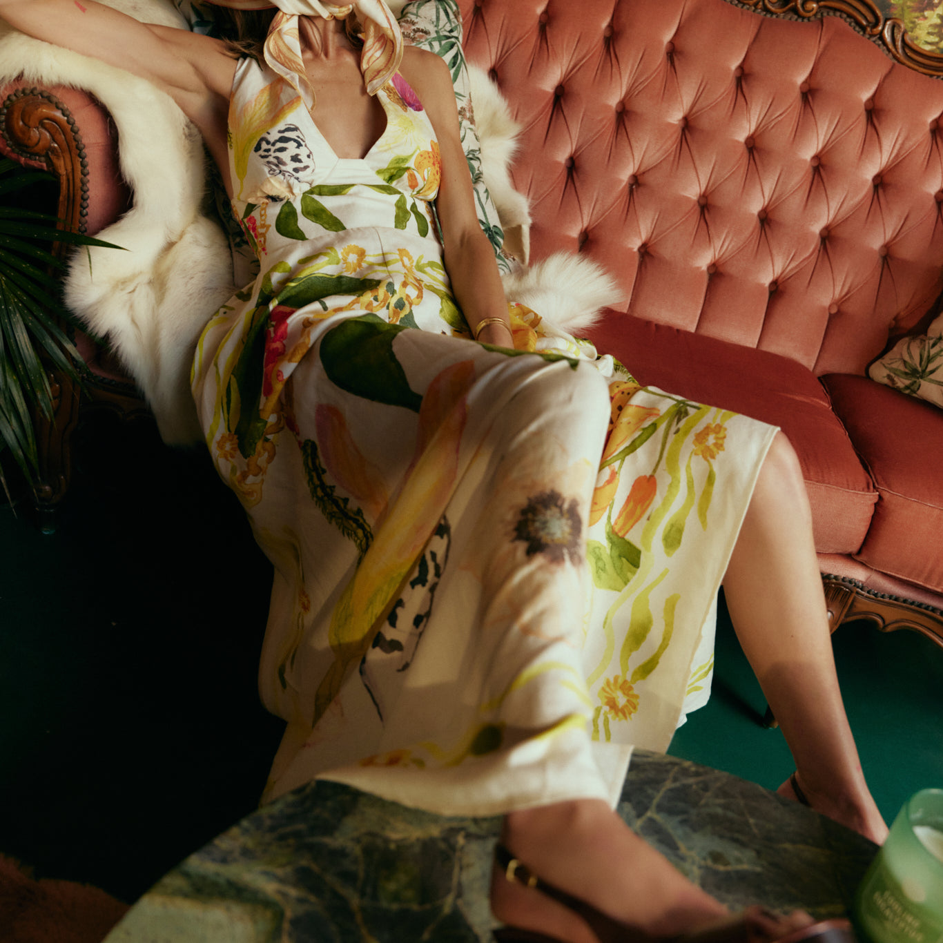 Woman in a floral dress sitting on a pink couch with a decorative background