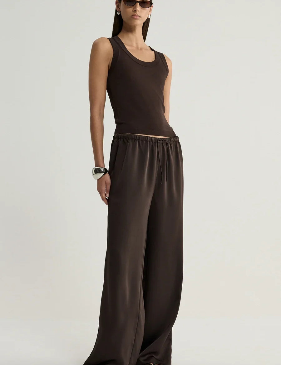 Model wearing the Elka Collective Mina Satin Pant in chocolate brown, featuring a relaxed wide-leg silhouette and elastic waistband, styled with a matching tank top. or hayes knit top 
chocolate brown satin pants, relaxed, wide-leg, adjustable waist, true to size for a relaxed fit. 